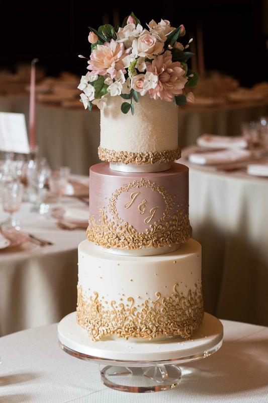 An opulent three tier wedding cake with sugar flowers and elaborate handpiped gold decoration at Peckforton Castle in Cheshire
