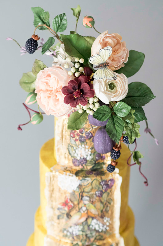 Saffron yellow wedding cake with a hand-painted chinoiserie style panel featuring two love birds surrounded by summer fruits, birds and butterflies.