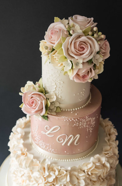 Efflorescence wedding cake design. Pretty three-tiered wedding cake in ivory and shimmering pink with ivory ruffles, pale pink roses and delicate lace detail.  Yorkshire wedding cake